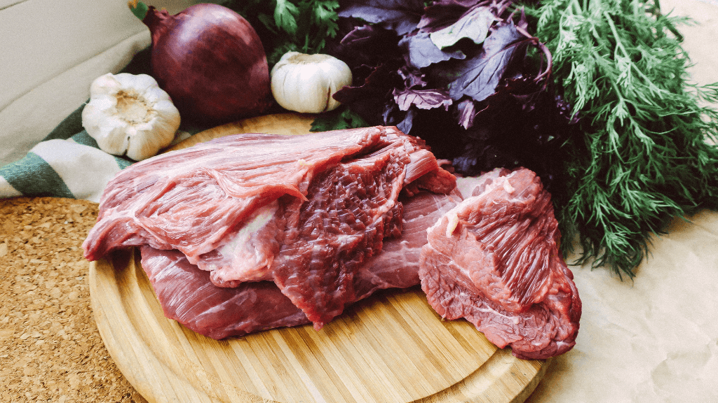mięso surowe na drewnianej desce, obok warzywa